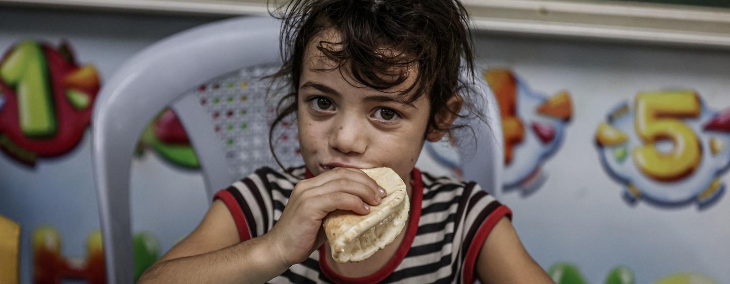 Une jeune fille mange du pain distribué par le Programme alimentaire mondial dans une école de l'UNRWA à Gaza. 