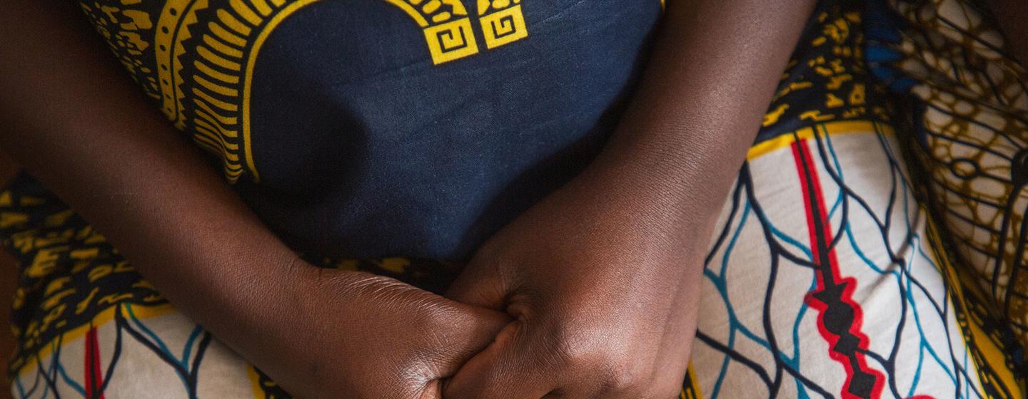 Gros plan sur les mains d'une femme jointes sur ses genoux, assise à l'hôpital Panzi de Bukavu.