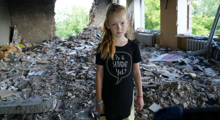 Восьмилетняя девочка стоит посреди руин свой школы в Украине.