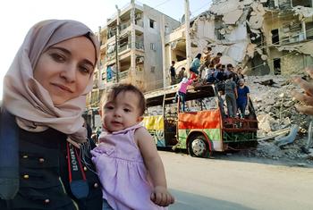 Waad Al-Kateab stands in front of a bombed-out building in Syria with her daughter in her arms.