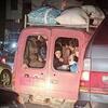 Un groupe de personnes déplacées, y compris des femmes et des enfants, sont entassées à l'arrière d'une camionnette rouge chargée de bagages sur le toit, illustrant la crise humanitaire au Liban.