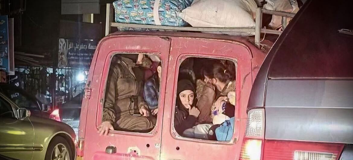 Un groupe de personnes déplacées, y compris des femmes et des enfants, sont entassées à l'arrière d'une camionnette rouge chargée de bagages sur le toit, illustrant la crise humanitaire au Liban.