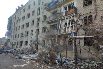 A view of a heavily damaged multi-story brick apartment building in Sloviansk, Ukraine, with debris scattered on the street in front.