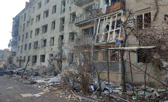 A view of a heavily damaged multi-story brick apartment building in Sloviansk, Ukraine, with debris scattered on the street in front.