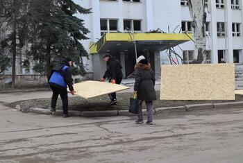 Civilians carrying large sheets of plywood in front of a damaged building in Sloviansk, Ukraine, as part of reconstruction efforts.