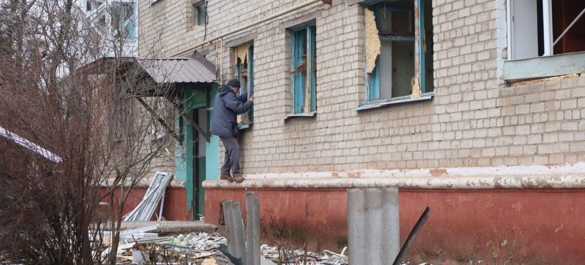 A man inspects the damage to a brick apartment building in Sloviansk, Ukraine, with broken windows and debris scattered on the ground.