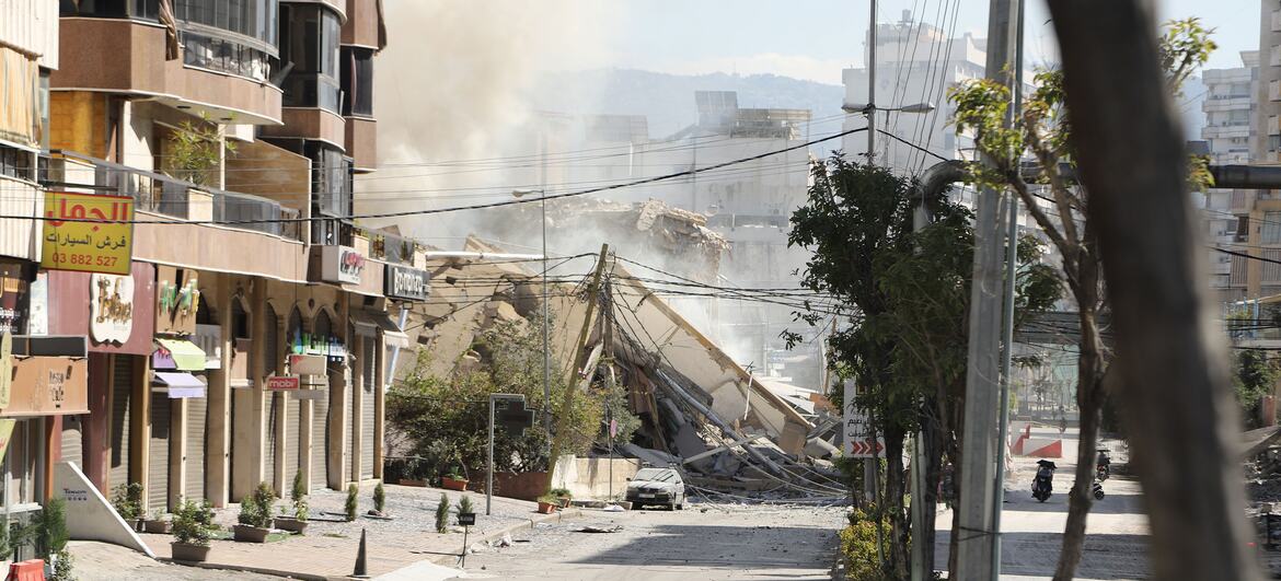 Uma rua em Dahiyeh, subúrbio sul de Beirute, Líbano, em 9 de março de 2026, mostrando as consequências de ataques aéreos com um grande edifício desmoronado, escombros e nuvens de poeira.