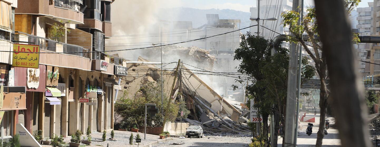 Une rue à Dahiyeh, dans la banlieue sud de Beyrouth, au Liban, le 9 mars 2026, montrant les conséquences des frappes aériennes avec un grand bâtiment effondré, des décombres et des nuages de poussière.
