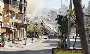 Una calle en Dahiyeh, suburbios del sur de Beirut, Líbano, el 9 de marzo de 2026, que muestra las consecuencias de los ataques aéreos con un gran edificio derrumbado, escombros y nubes de polvo.