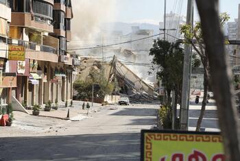 Une rue à Dahiyeh, dans la banlieue sud de Beyrouth, au Liban, le 9 mars 2026, montrant les conséquences des frappes aériennes avec un grand bâtiment effondré, des décombres et des nuages de poussière.