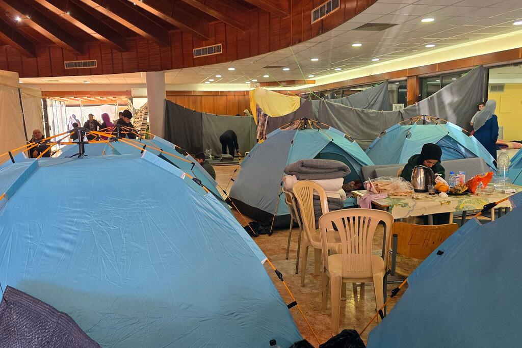 Une équipe de l'OMS inspecte un abri temporaire avec des tentes bleues et des personnes à l'intérieur, géré par Caritas Liban à l'Institut technique Dekwaneh de Beyrouth, au Liban, le 9 mars 2026.