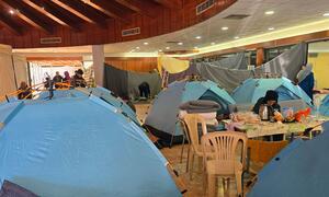 WHO team inspects temporary shelter with blue tents and people inside, run by Caritas Lebanon at Dekwaneh Technical Institute in Beirut, Lebanon, on March 9, 2026.