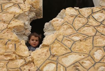 A young Syrian boy peeks through a hole in a damaged stone wall in Saraqab, Idlib, during Eid Al-Fitr celebrations on April 1, 2025.