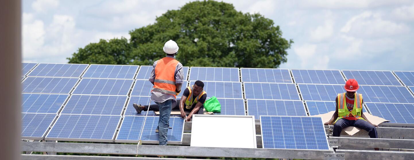 Des ouvriers installent des panneaux solaires sur une structure métallique en Tanzanie.