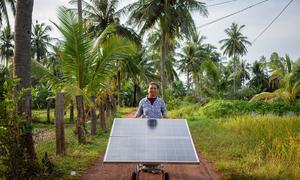 Un miembro de un grupo de mujeres agricultoras de Camboya hace rodar un panel solar por un sendero.