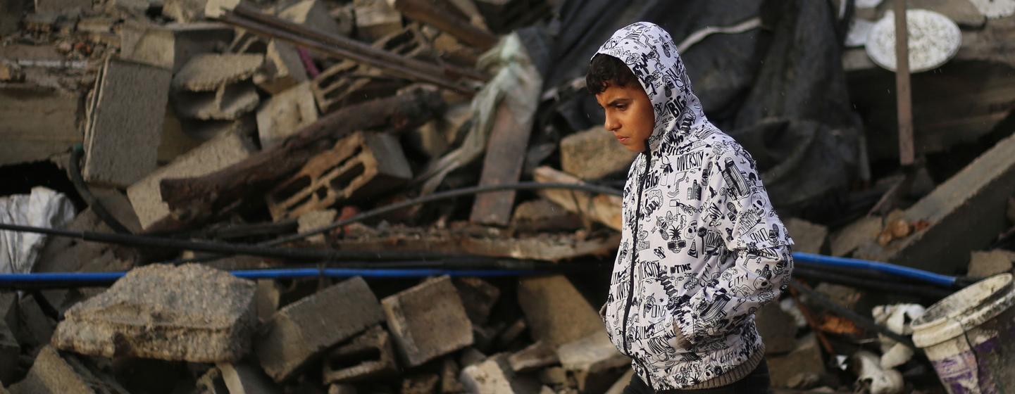 在加沙地带南部的拉法市，一名男孩走过被毁房屋的废墟。
