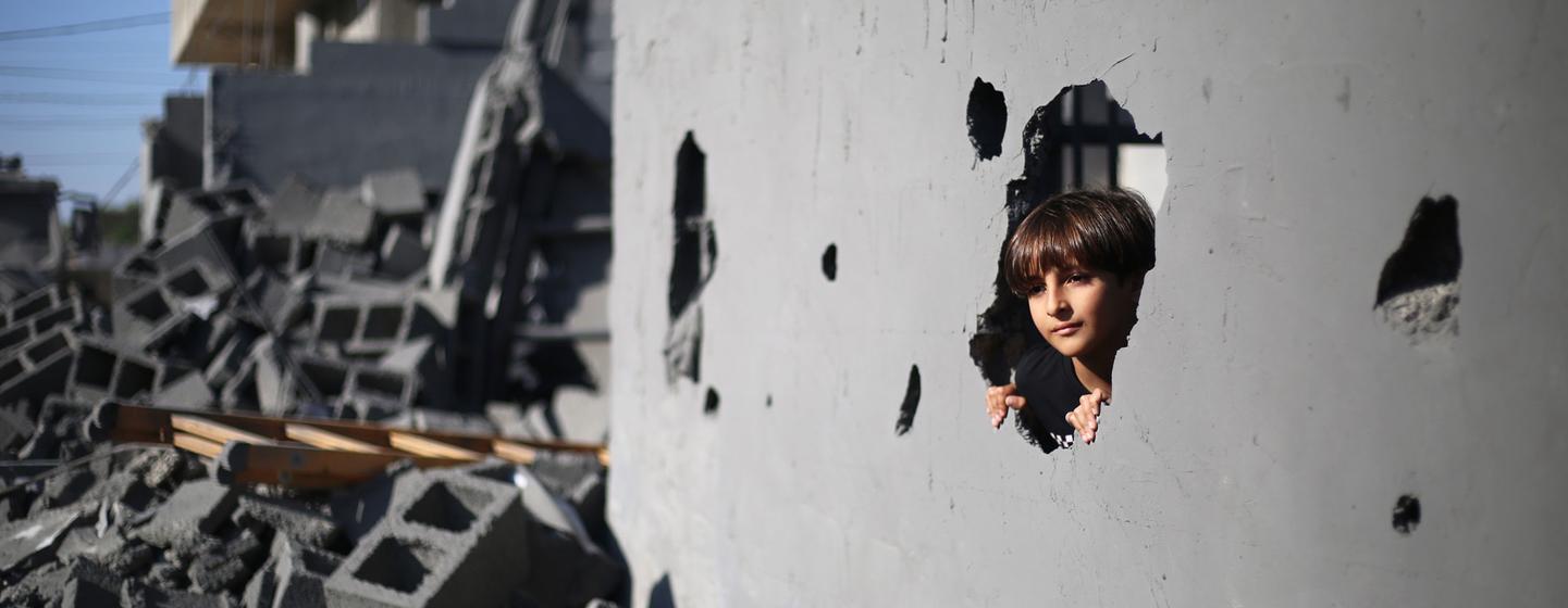 加沙地带南部的拉法，一名 10 岁男孩正在透过自家墙上因空袭造成的洞往外看。