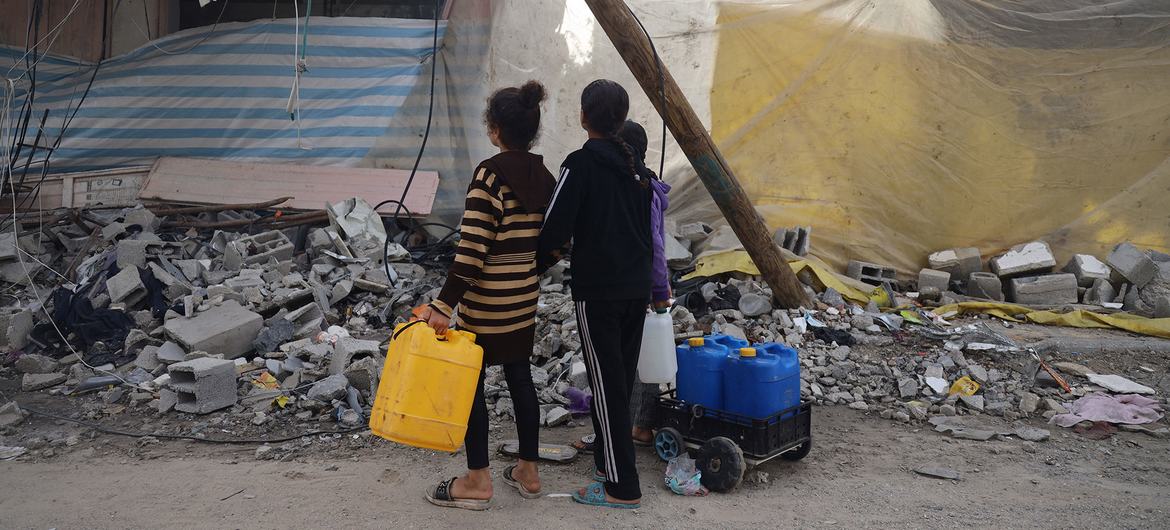 Children in Khan Younis stop to look at the destruction as they go in search for water.