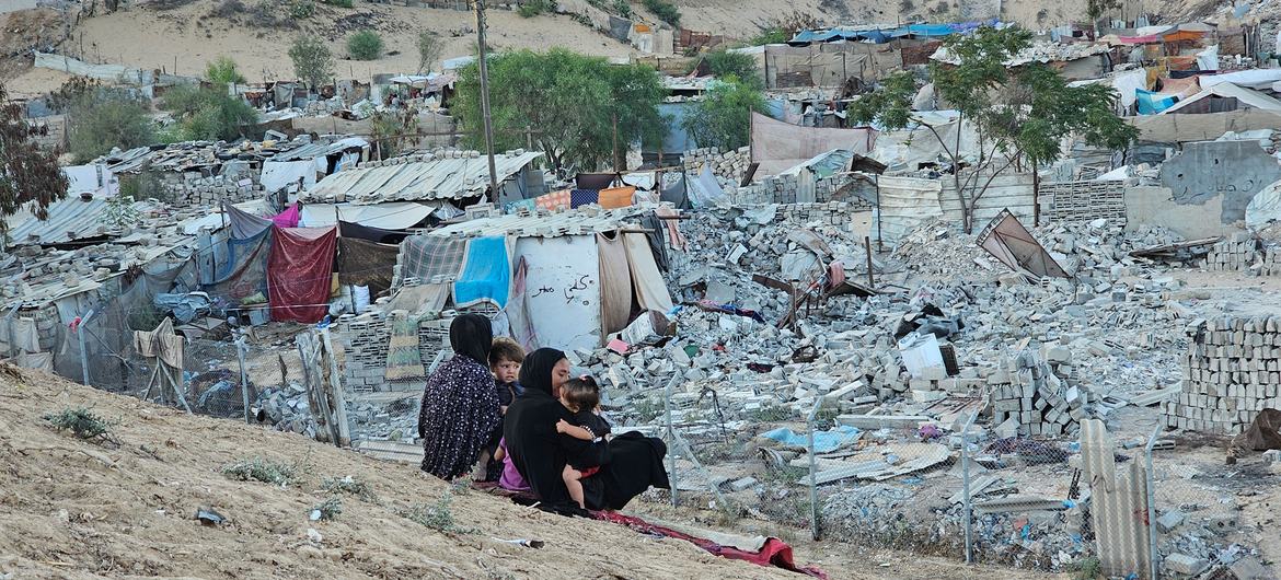 Des femmes et des enfants sont assis sur une colline surplombant un quartier détruit à Gaza.