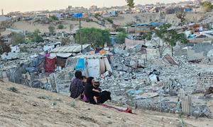 Women and children sit on a hill overlooking a destroyed neighbourhood in Gaza.