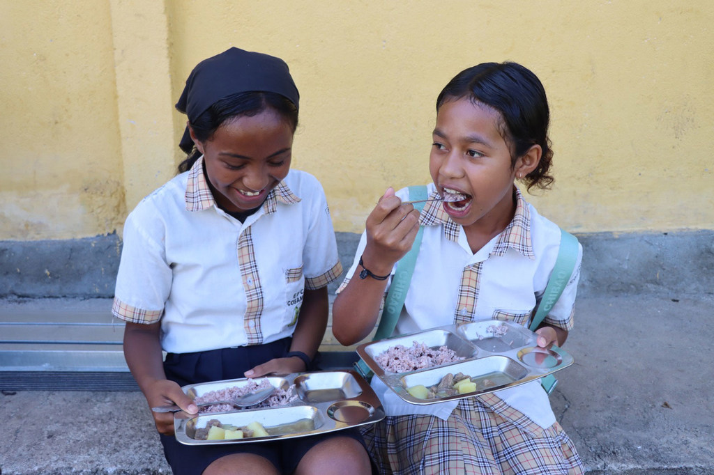Two girls east a hot meal prepared at school o Timor-Leste.