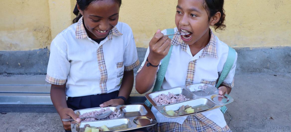 © WFP/Isabel Pereira Two girls east a hot meal prepared at school o Timor-Leste.