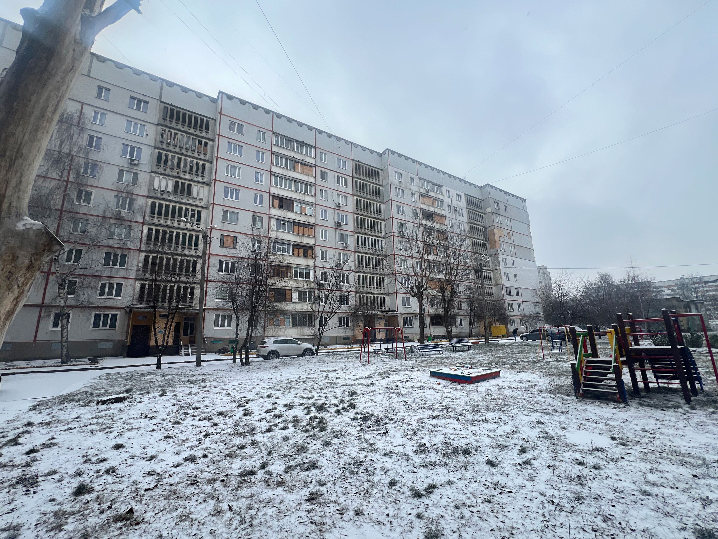 Des immeubles d'appartements endommagés à Saltivka, Kharkiv, en Ukraine, avec un terrain recouvert de neige et un terrain de jeux en premier plan.