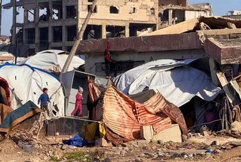 Les enfants marchent près de tentes improvisées placées parmi les décombres et les bâtiments détruits le long de la plage de Gaza, soulignant les conditions de vie difficiles des Palestiniens déplacés.