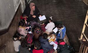 Un maestro guía a los niños palestinos mientras estudian juntos en un aula improvisada en Gaza, destacando los esfuerzos de la UNRWA para proporcionar educación a pesar de las escuelas destruidas.