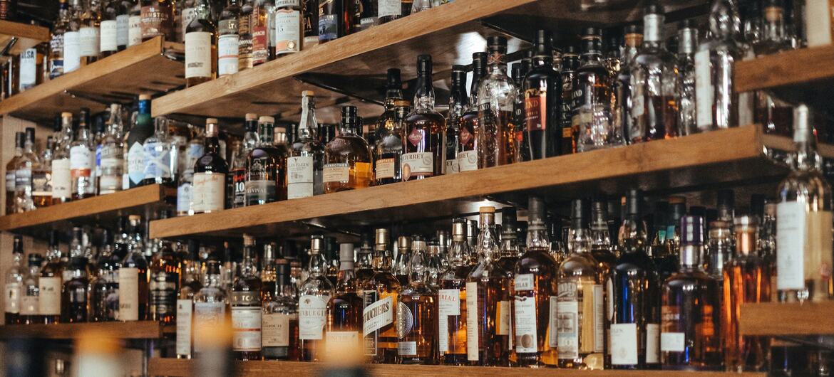 Una vista de cerca de numerosas botellas de alcohol colocadas en estantes de madera en un bar.