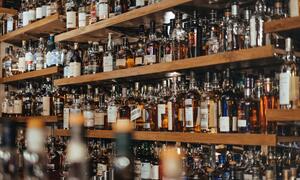 Una vista de cerca de numerosas botellas de alcohol colocadas en estantes de madera en un bar.