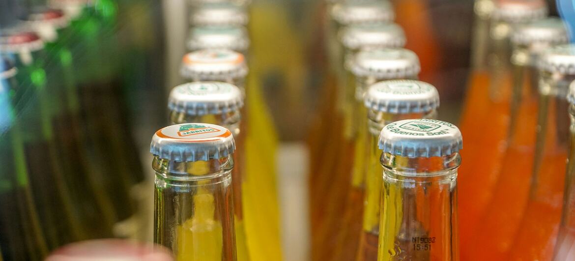 Rows of colorful fruit juice bottles displayed in a refrigerated case at a supermarket.