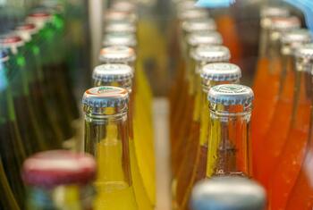 Rows of colorful fruit juice bottles displayed in a refrigerated case at a supermarket.