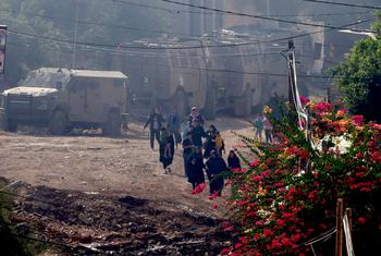 Palestinian families and children walk past destroyed buildings and parked military vehicles in the Jenin refugee camp.