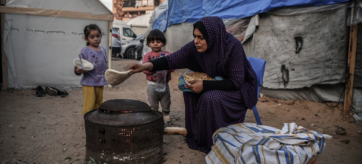 Uma mãe prepara uma refeição para seus filhos do lado de fora de sua casa improvisada em um campo de refugiados em Khan Younis, Gaza.