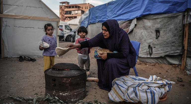 Uma mãe prepara uma refeição para seus filhos do lado de fora de sua casa improvisada em um campo de refugiados em Khan Younis, Gaza.