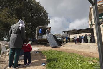 एक महिला और एक बच्चा लेबनान में एक ट्रक से एक गद्दे को उतारते हुए देख रहे हैं।