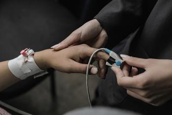 Una mujer sostiene la mano de un niño con una venda intravenosa en el brazo mientras conecta un oxímetro de pulso a su dedo.
