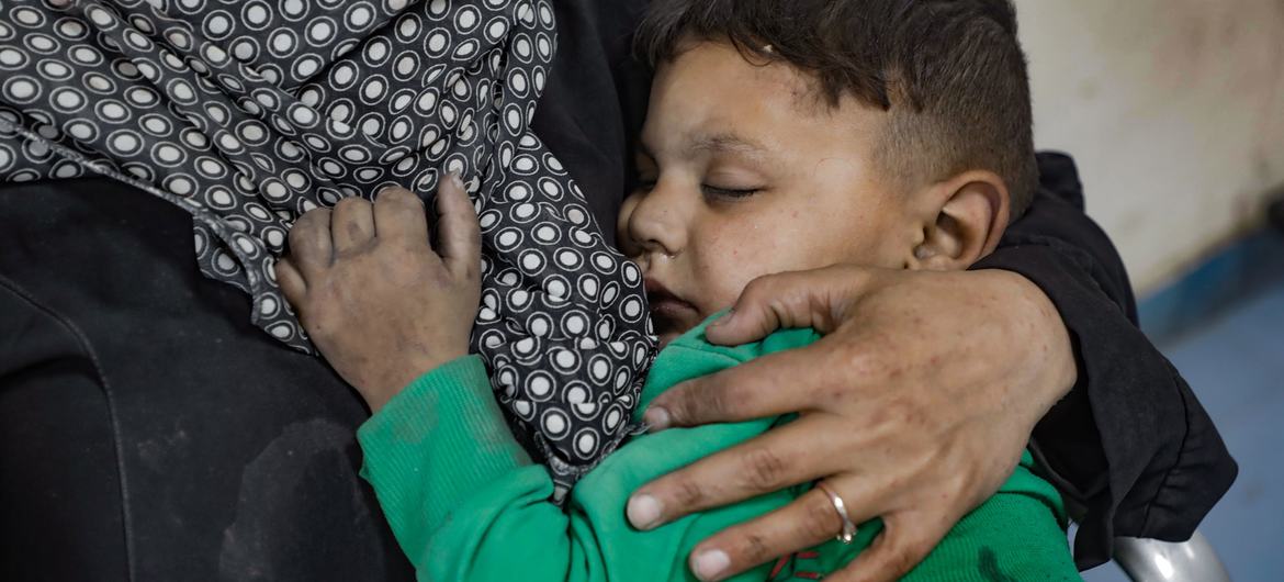 A young boy, injured in an attack on Dar Al-Arqam School in Gaza, is being comforted by an adult in a hospital setting.