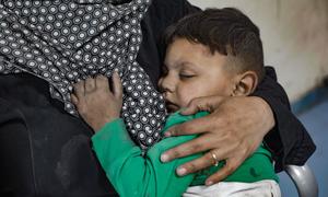 A young boy, injured in an attack on Dar Al-Arqam School in Gaza, is being comforted by an adult in a hospital setting.