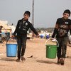 सीरिया के इदलिब में, विस्थापित लोगों के लिए बनाए गए एक शिविर में, पानी भर कर ले जाते हुए दो बच्चे.