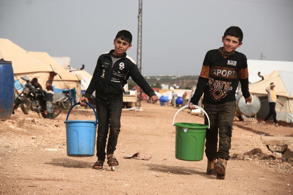 Deux enfants portent de l'eau dans un camp de déplacés à Idlib, en Syrie (photo d'archives).