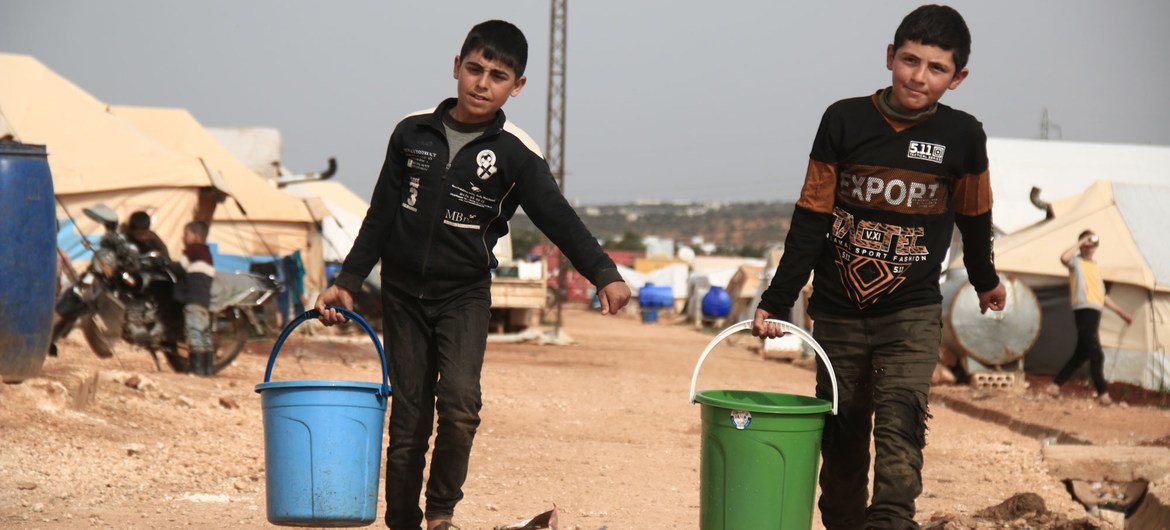 Duas crianças coletam água potável em um campo para deslocados em Idlib, na Síria.