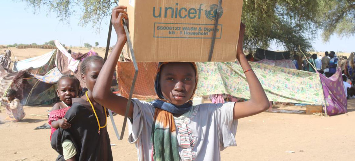 Uma jovem porta um kit "WASH & Dignity" distribuído pela UNICEF na cabeça num campo de refugiados em Tawila, no Sudão, onde famílias fugiram da violência de Al Fasher.