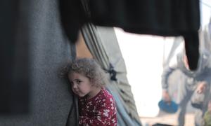 A young girl peers out from a tent in Gaza.