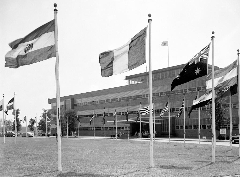 Черно-белая фотография временного штаб-квартиры Организации Объединенных Наций в озере Success, с флагами 60 государств-членов, летящих на 20-метровых полях перед главным входом.