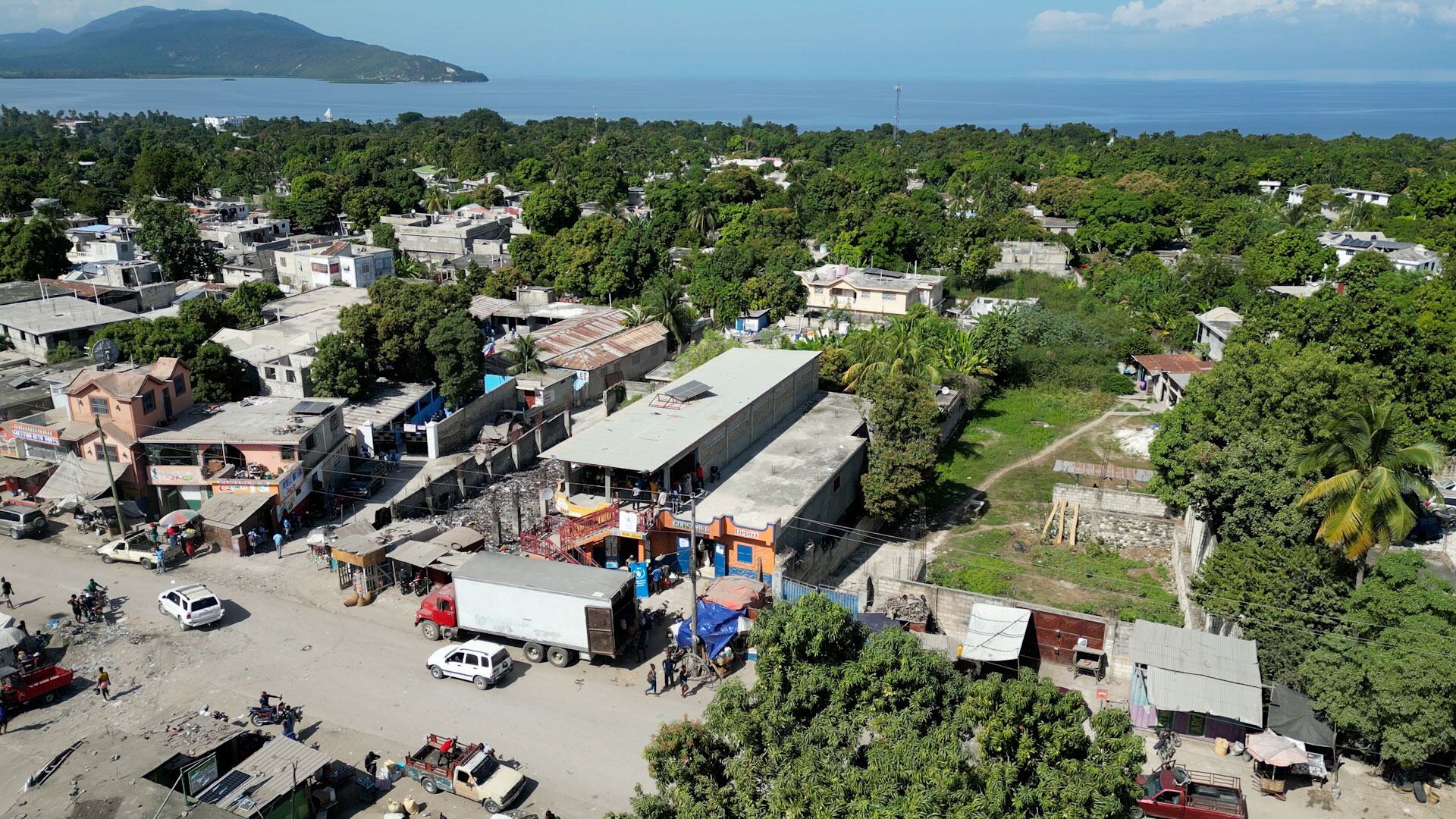 Une vue aérienne d'une communauté haïtienne touchée par une tempête, montrant des maisons, des routes et des véhicules, le PAM fournissant une aide alimentaire par le biais d'un système de coupons.
