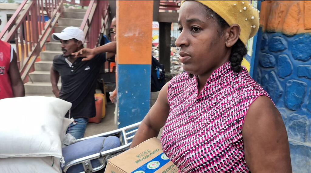 A woman in Haiti, identified as Ketia, is seen holding a box of aid supplies received through the World Food Programme's voucher system, which helps families purchase goods from local retailers after a storm.