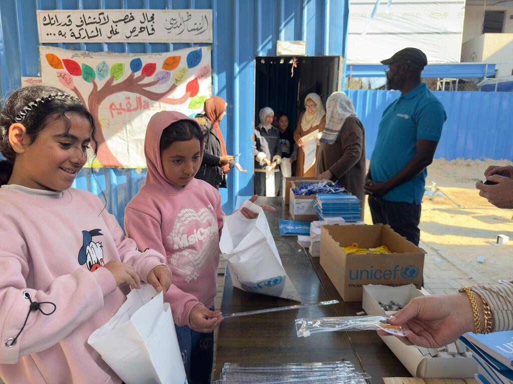 Deux jeunes filles palestiniennes en pull-over rose reçoivent des fournitures scolaires dans une boîte de l'UNICEF à Deir El Balah, à Gaza. La scène montre des boîtes de matériel pédagogique distribuées pour soutenir l'apprentissage en période de crise.