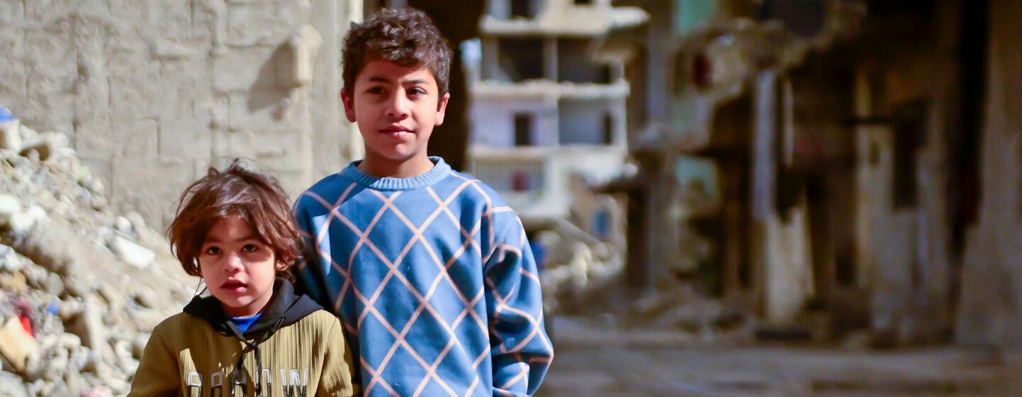Deux jeunes enfants syriens, Rami (10) et Noureddine (4), se tiennent devant des bâtiments endommagés dans le quartier Al-Tadamon de Damas, en Syrie.Le projet de réhabilitation des eaux usées soutenu par l'UNICEF, financé par le gouvernement allemand par l'intermédiaire de la KfW Development Bank, a amélioré la sécurité et les conditions de vie des familles de la région.